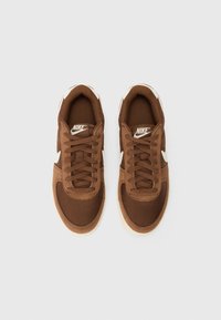 Bruine sneaker met een getextureerde bovenkant, witte Nike swoosh, zes veterogen en een lichtbruine rubberen zool. Beschikt over een gevoerde kraag en tong.
