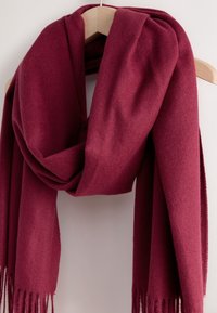 Bordeauxroter Wollschal, der an einem Holzkleiderbügel hängt, mit weicher Textur und langen Fransen an beiden Enden.