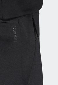 Svarta träningsbyxor gjorda av ett slätt, stretchigt material; har en dragkedjeförsedd sidoficka och ett tryckt "CLIMATITE"-logotyp på framsidan.