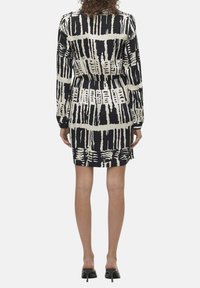 Robe noire et crème avec manches longues, taille cintrée et motif abstrait, présentant une coupe droite et un ourlet à la hauteur du genou.