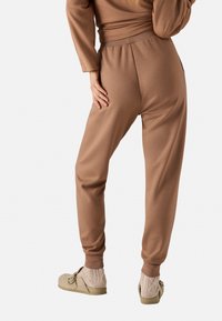 Pantalones sudadera marrones con piernas ajustadas, cintura elástica y bolsillos laterales, combinados con zapatos beige de tipo slip-on y calcetines de punto hasta el tobillo.