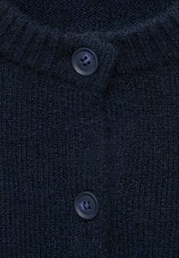 Mörk marinblått stickat tyg med två svarta knappar sydda i en vertikal linje, som visar ribbad textur och mjukt material.