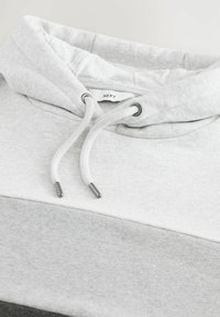 Hellgrauer und weißer Hoodie mit Farbblock-Design, Kordeln und einem sichtbaren "NEXT" Markenlabel im Halsausschnitt.