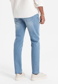 Vaaleansiniset farkut suoran mallin, takataskut ja hieman haalistunut ilme. Yhdistetty beigeihin tennareihin, kuvattuna sivulta ja takaa.