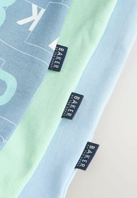 Trīs kokvilnas t-krekli gaiši zilā un piparmētru zaļā krāsā, ar grafisku dizainu un mazām zīmola etiķetēm uz tumši zilā fona.