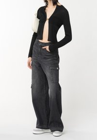 Gilet court côtelé noir avec fermeture éclair, associé à un pantalon cargo taille haute à jambe large en denim noir délavé. Baskets blanches.