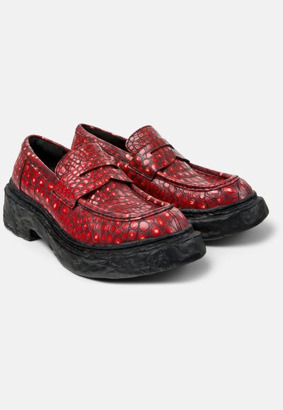Coppia di mocassini rossi con motivo a coccodrillo e suole nere spesse e testurizzate, esposti su sfondo bianco.