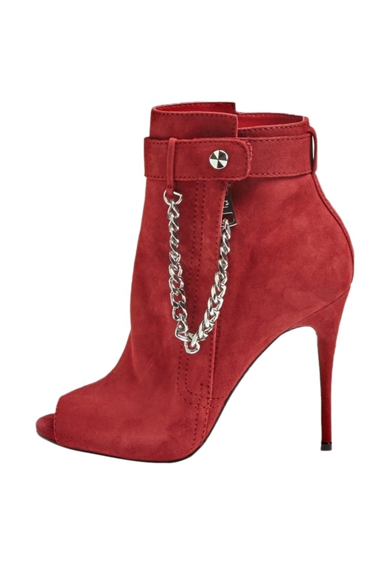 Bottine à talons hauts en daim rouge avec ouverture à l'avant, chaîne argentée décorative et bride avec fermeture à clous autour de la cheville.