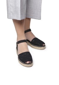 Svart virkade espadrillosandaler med rem runt vristen, vävd ovandel, öppen tå och detaljer i jute-sula. Lämpliga för vardagsbruk.