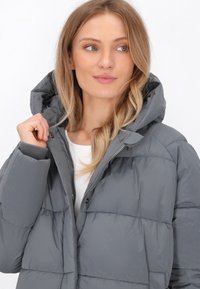 Jachetă puffer gri cu fermoar frontal și glugă. Prezintă cusături orizontale, manșete elastice și o textură de stofă netedă și lucioasă.