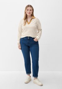 Striped long-sleeve shirt with a brown collar, paired with blue jeans. White sneakers on feet. Overall relaxed fit and casual style.