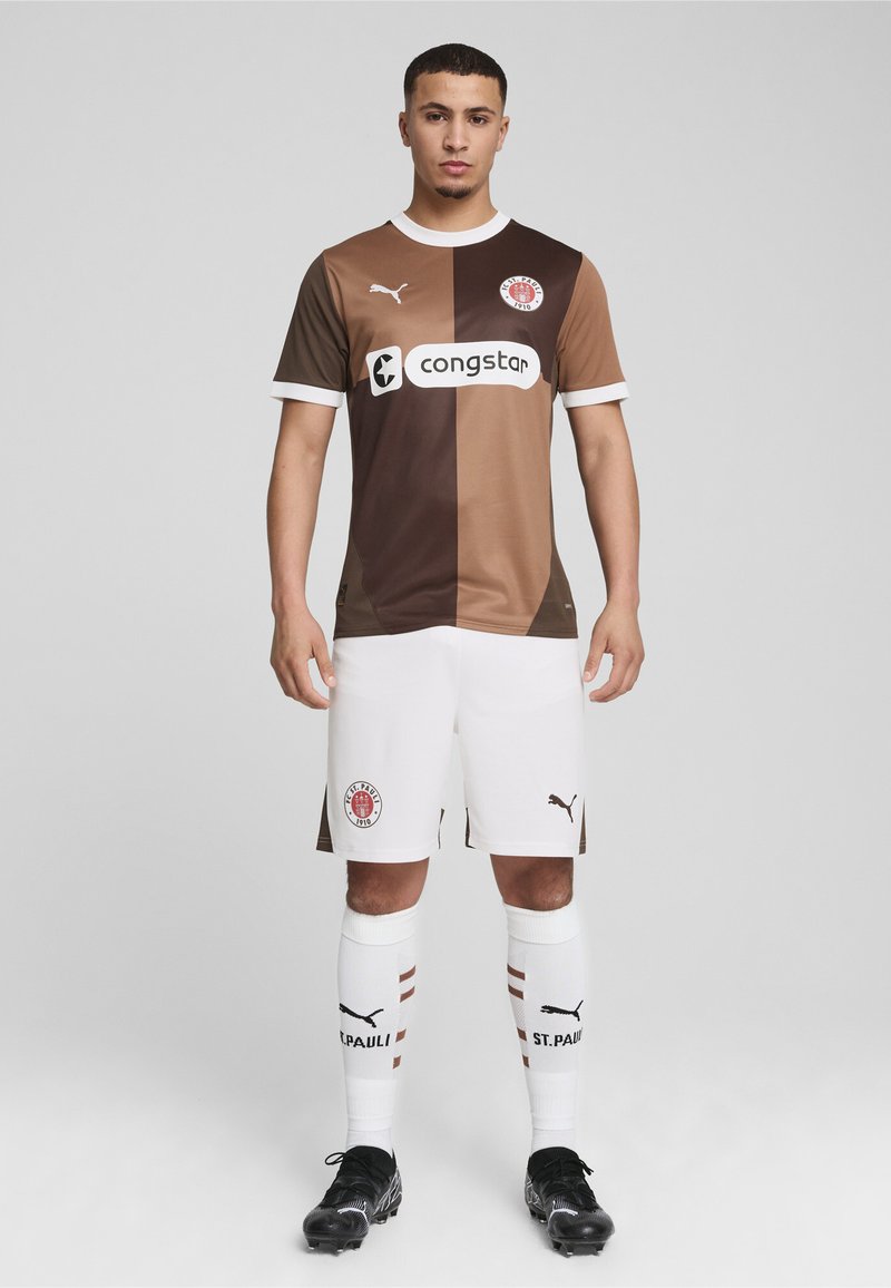 Pruun ja heledatpruun jalgpallijerseys valgete aktsentidega, logoga ja reklaamiga. Kombineeritud valgete lühikeste pükste ja sokkidega, millel on punased aktsendid. Mustad saapad.