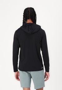 Haut à capuche noir à manches longues avec une coupe standard, featuring un capuchon avec cordon de serrage, une texture lisse et un détail de logo sur la manches gauche.
