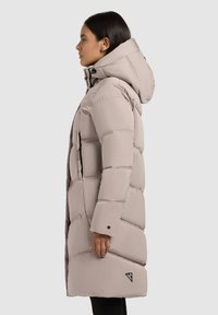 Pufjakas gaiši bež krāsā ar kapuci, pāršūtu dizainu un ar rāvējslēdzēju sānu kabatām. Ievērības cienīgs melns logotipa akcents sānos.