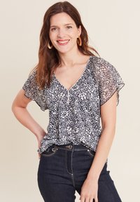 Marineblouse met wit bloemenpatroon, korte doorschijnende mouwen, V-hals en geplooide voorkant. Gecombineerd met donkere denim jeans.