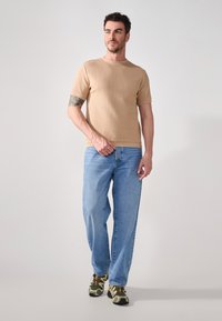 Beige, textured short-sleeve shirt paired with light blue jeans and green patterned sneakers. The outfit features a relaxed fit design.