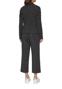 Černá texturovaná bunda v kombinaci s odpovídajícími zkrácenými kalhotami, nošena s bílými teniskami se stříbrnými akcenty. Pohled zezadu na outfit.