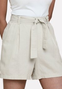 Pantaloncini beige chiaro realizzati in un tessuto testurizzato, con vita cinturata, pieghe frontali e tasche laterali.