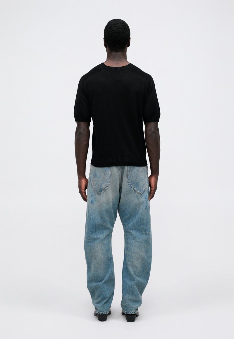 Maglietta a maniche corte nera in maglia abbinata a jeans larghi di colore blu chiaro. I jeans presentano toppe sbiadite e tasche posteriori con cuciture curve.