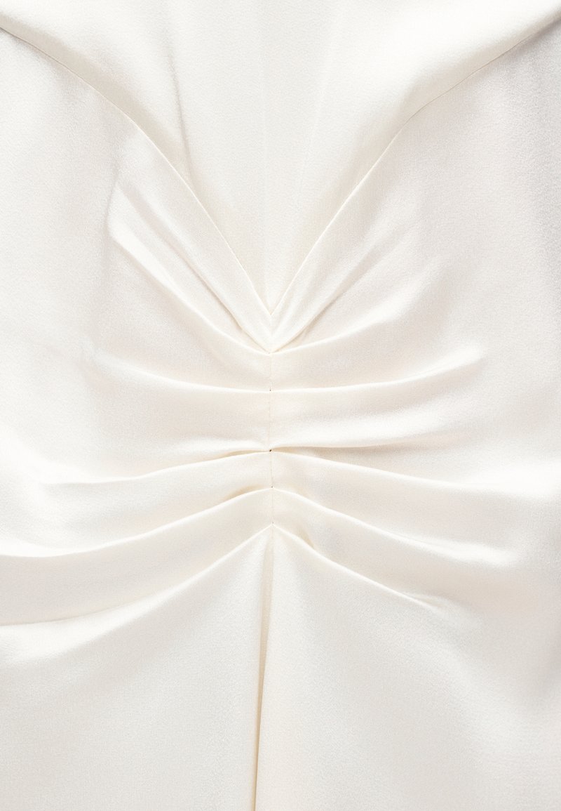 Gros plan d'un tissu satin ivoire avec des détails froncés et plissés créant des plis symétriques et un éclat doux.