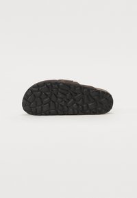 Zwarte rubberen sandaalzool met een gestructureerde, patroonachtige grip. Afgeronde vorm, stevig materiaal en lichte boog voor comfort.