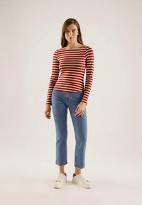 Rød og kremstripet langermet skjorte kombinert med lyseblå cropped jeans. Modellen har på seg hvite joggesko og hoops-øredobber.