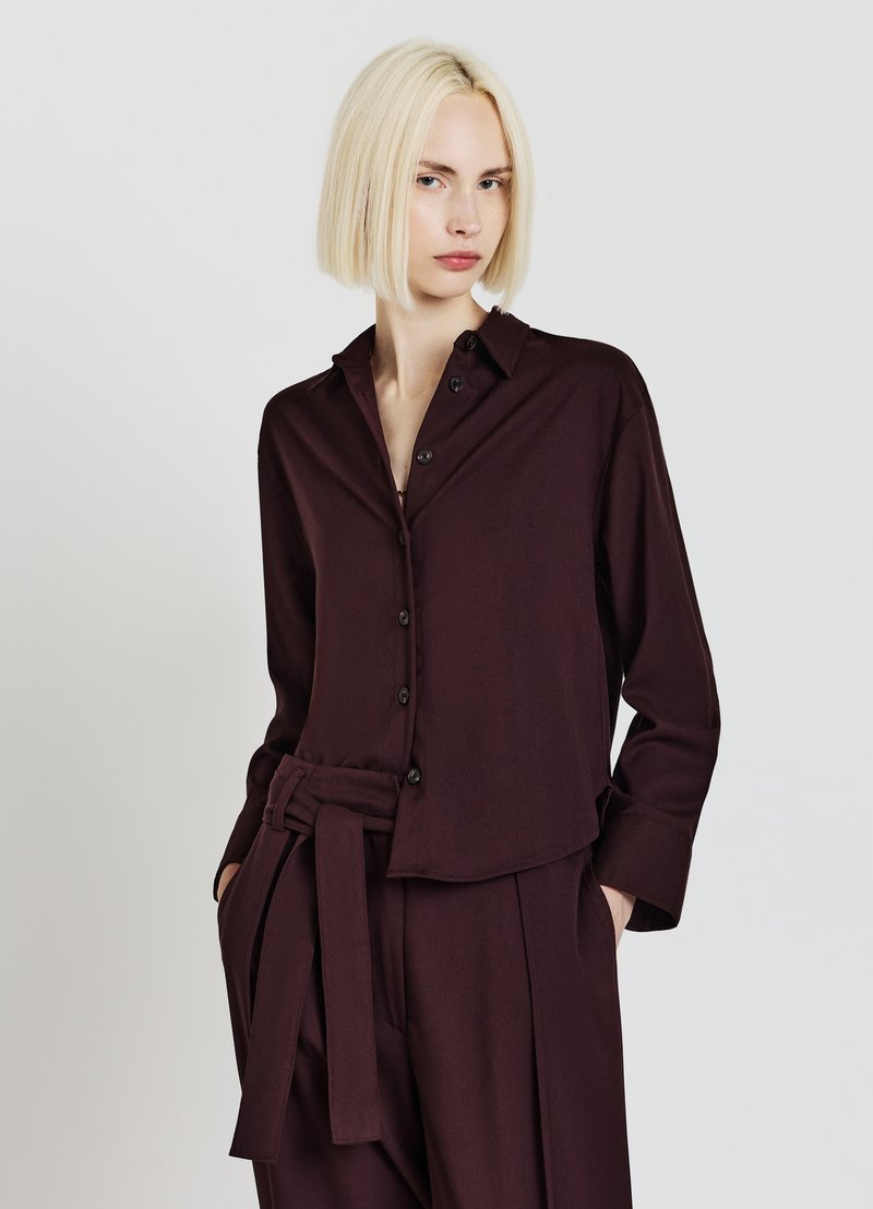 Chemise bordeaux à manches longues avec une fermeture à boutons sur le devant, un col et une coupe décontractée. Comprend une ceinture assortie et une texture de tissu douce.