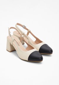 Tacchi slingback beige e neri con tacco a blocco, punta appuntita e lati intagliati. Le scarpe presentano una fascia sling con fibbia regolabile.