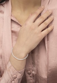 Silver bracelet with a curved design, featuring a row of small, clear rhinestones, worn on a hand against a pink satin blouse.