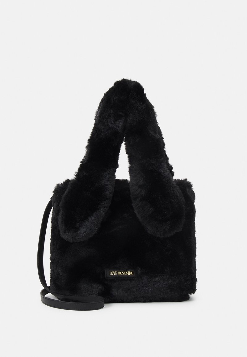 Černá kabelka z imitace kožešiny s měkkou texturou, obdélníkovým tvarem a zaoblenou rukojetí. Obsahuje odnímatelný černý popruh a zlatý detail s logem.