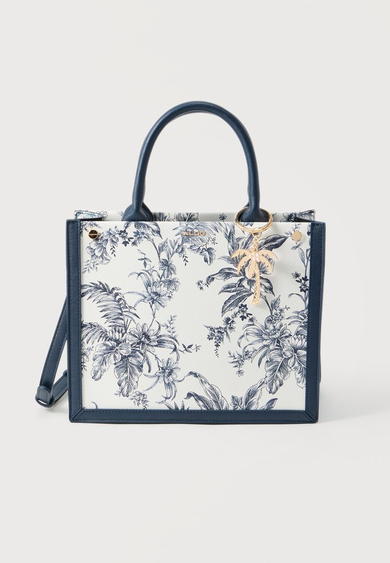 White tote bag with navy blue floral print, navy trim and handles, gold palm tree keychain, and detachable shoulder strap.