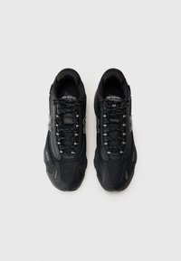 Svarte sportsko med mesh-overdel, teksturert, reflekterende detaljer og forsterket tåboks. Har et fast snøresystem for sikker passform.