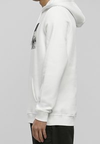 Sudadera blanca con capucha hecha de tela suave, con un bolsillo tipo canguro y un estampado gráfico en el pecho. Puños y dobladillo acanalados completan el diseño.