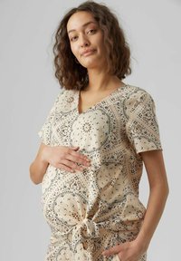 Top maternità in tessuto beige chiaro con stampa paisley, maniche corte, scollo a V e dettaglio nodo frontale in vita, che mette in evidenza una vestibilità comoda.