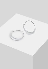 Pendientes de aro de plata con un diseño suave y curvado. Tienen un acabado pulido y un cierre sin costuras, reflejando la luz de manera eficiente.
