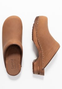 Brown leather clogs feature a smooth finish, rounded toe, and wooden heel. Stitching detail accents the side of each shoe.