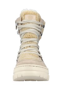 Bota beige clara con cordones, forrada con un suave pelo texturizado, cuello acolchado y una suela gruesa blanca. Presenta herrajes plateados y cordones gruesos.