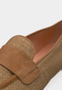 Κοντινό πλάνο ενός υφαντού καφέ μοκασίνι με λεπτομέρεια σουέιντ λουριού και λείο εσωτερικό επένδυση.