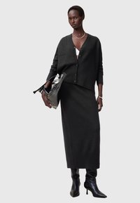 Mörkgrå stickad kofta med knappar, ihopparad med en matchande lång kjol. Svarta spetsiga högklackade stövlar och en transparent handväska.