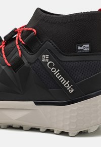 Svart Columbia vattentät sko med texturerad ovandel, röda snören och en tydligt geometrisk gummisula. Har en framträdande logotyp.