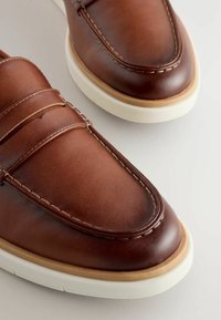 Mocassins en cuir marron avec surpiqûres décoratives, semelle en caoutchouc et texture lisse. Présentent un bout arrondi et un design minimaliste.
