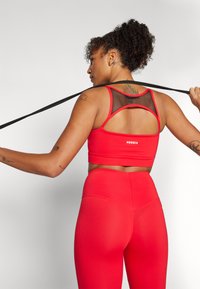Sujeción roja deportiva con una espalda de malla y un ajuste cómodo, combinada con leggins rojos de tiro alto que presentan un diseño sin costuras.