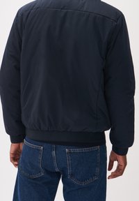 Giubbotto bomber trapuntato blu navy con orlo e polsini a costine, che mostra una superficie di tessuto liscia e un design semplice; indossato con jeans in denim.