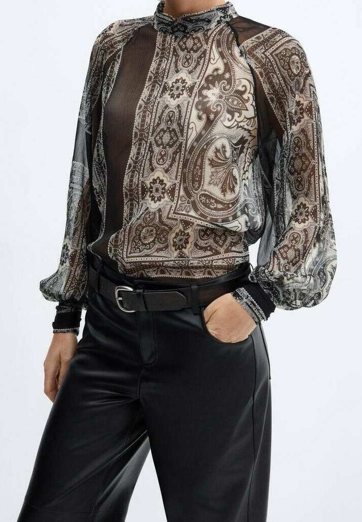 Blusa trasparente nera e bianca con motivi paisley, colletto alto e maniche a sbuffo. Abbinata a pantaloni in pelle nera a vita alta.