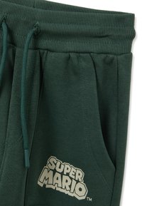 Pantaloni jogger in cotone verde scuro con fascia in vita a coste, coulisse regolabile, tasche laterali e logo "SUPER MARIO" color crema sul davanti.