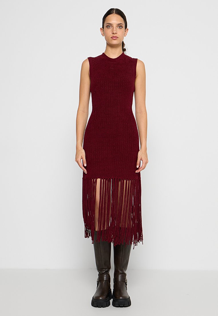 Vestido burdeos sin mangas con tejido de punto texturizado, que presenta un dobladillo largo con flecos y aberturas laterales, combinado con botas marrones hasta la rodilla.