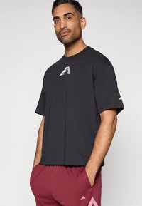 Čierne tričko s krátkym rukávom a okrúhlym výstrihom, s bielym logom na hrudi, v kombinácii s bordovými športovými šortkami s bočnou kapsou.