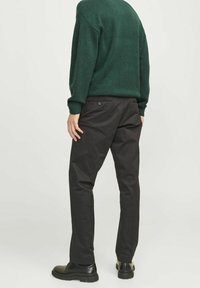 Schwarze Hosen mit geradem Schnitt, aus glattem Stoff, mit zwei Gesäßtaschen, kombiniert mit einem grünen Pullover und schwarzen Schuhen.