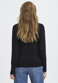 Suéter negro de manga larga con dobladillo acanalado, combinado con jeans de denim azul de cintura alta. La tela parece suave y ligera.