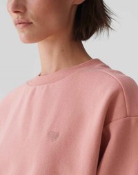 Felpa rosa chiaro con collo rotondo, texture morbida e un piccolo dettaglio di cuore ricamato sul petto. Vestibilità rilassata.